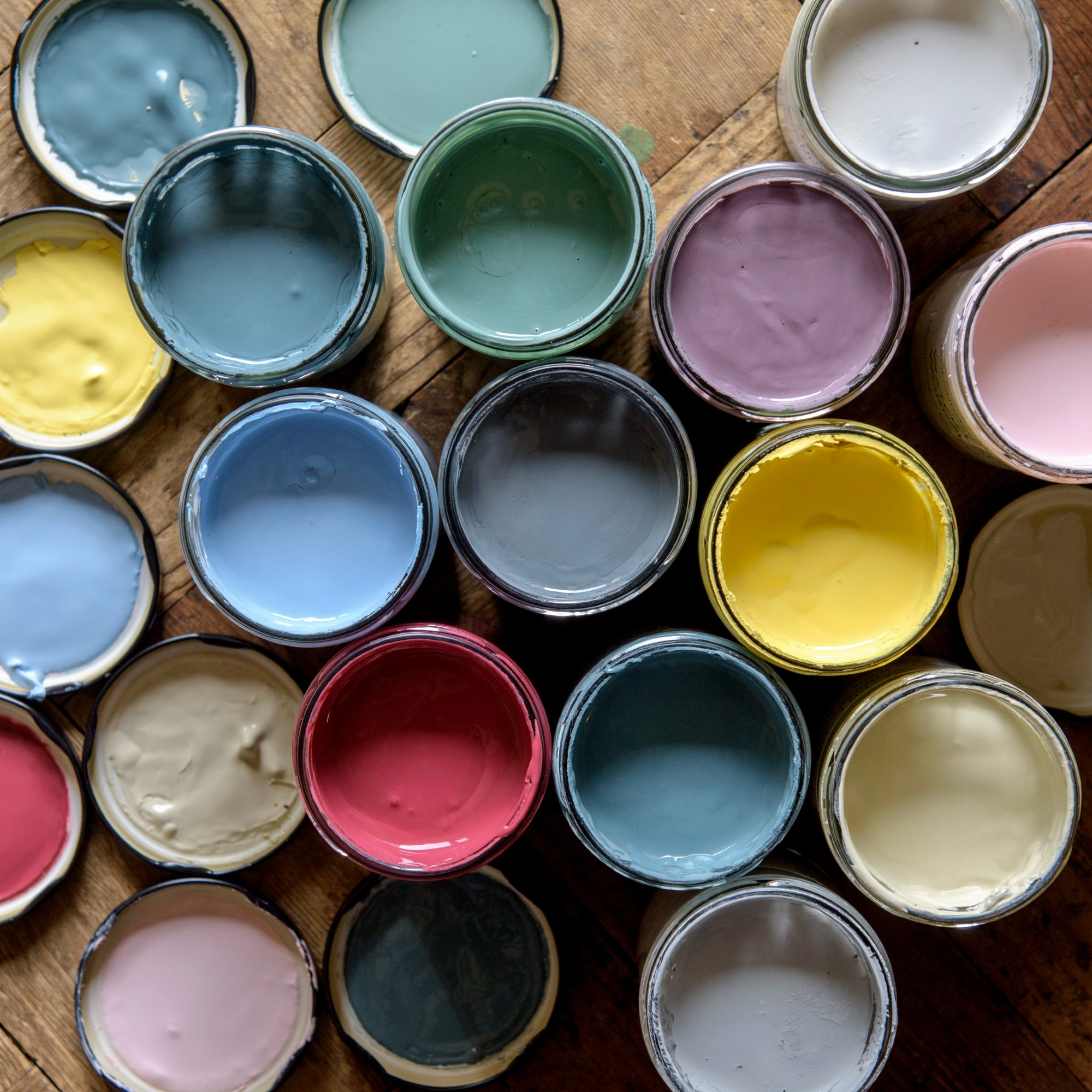Open jars of paint in various colours on wooden flooring