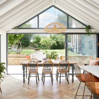 dining area in glazed extension with wooden farmhouse furniture and herringbone wood flooring