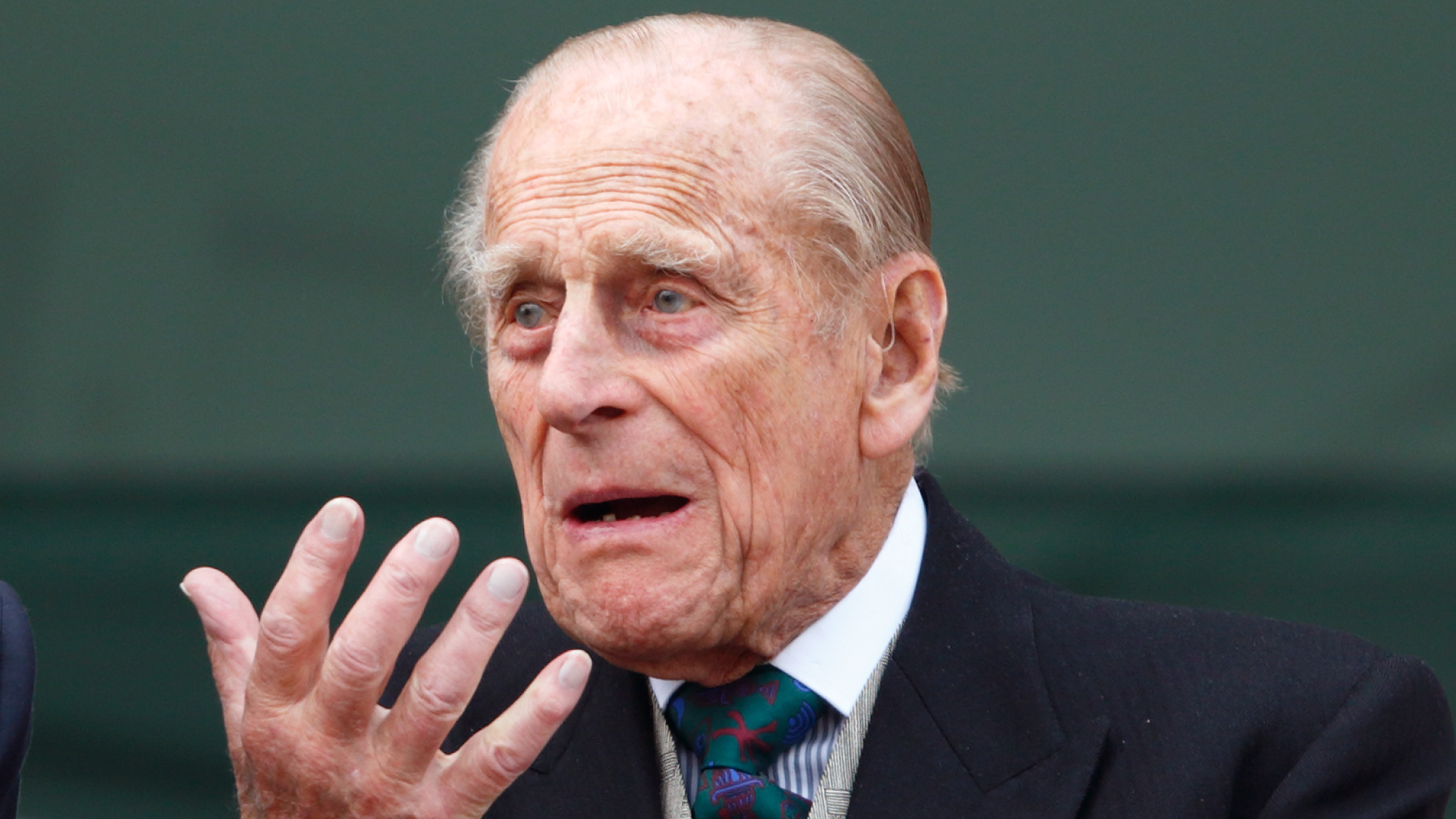 Prince Philip gestures with his hand while wearing a suit and tie