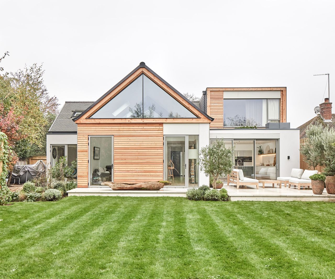 The rear exterior of a house with a lush green lawn and a contemporary self build home. The glazing is bespoke, and the cladding is timber