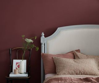 dark pink wall behind white headboard with pink bedding on bed, wooden chair next to bed being used as bedside table