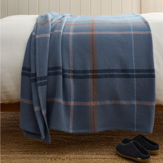 blue plaid throw blanket on a white bed and blue slippers