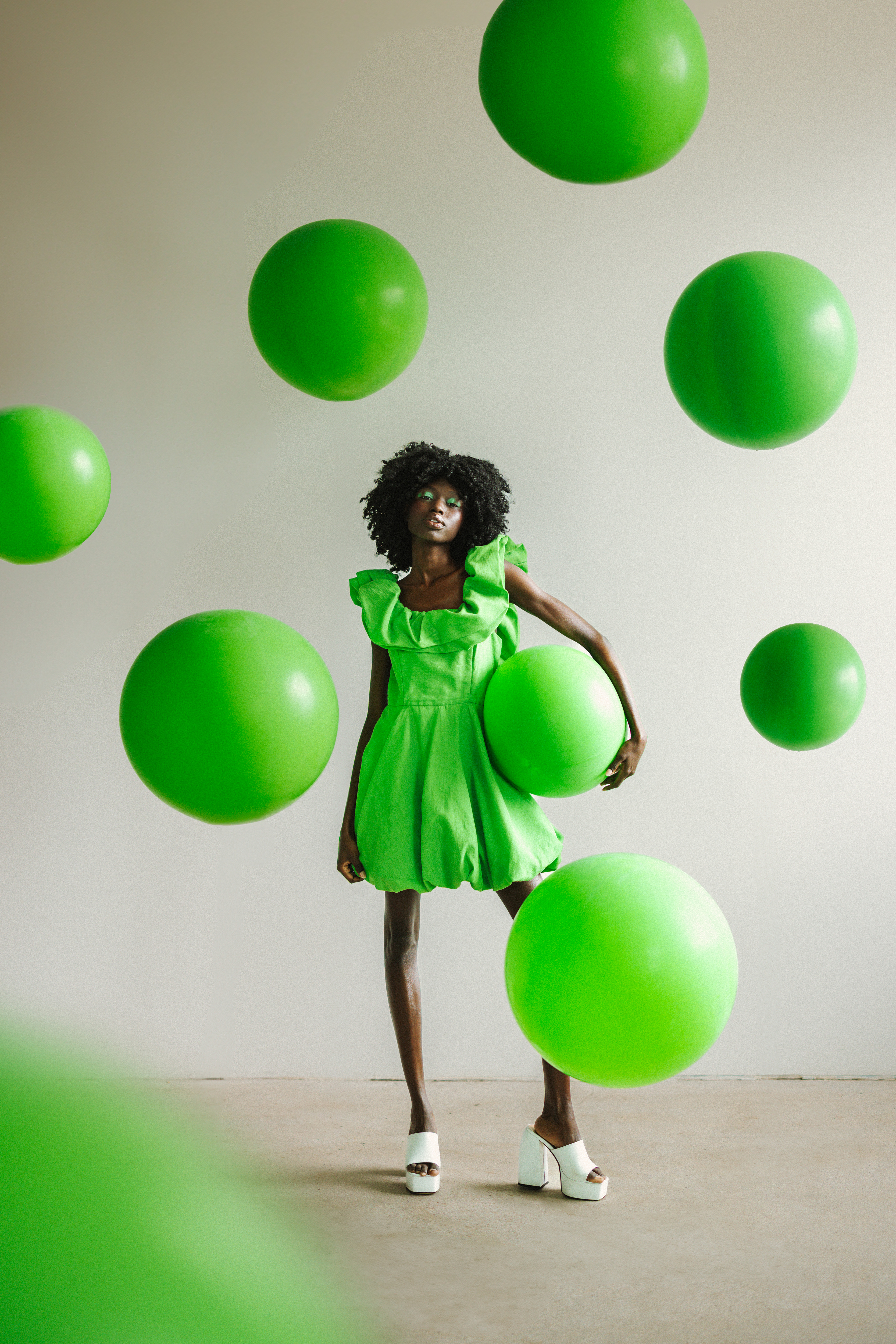 A colorful photograph of a woman in a green ress surrounded by green balloons