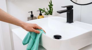 Woman cleaning a bathroom sink with a microfibre cloth