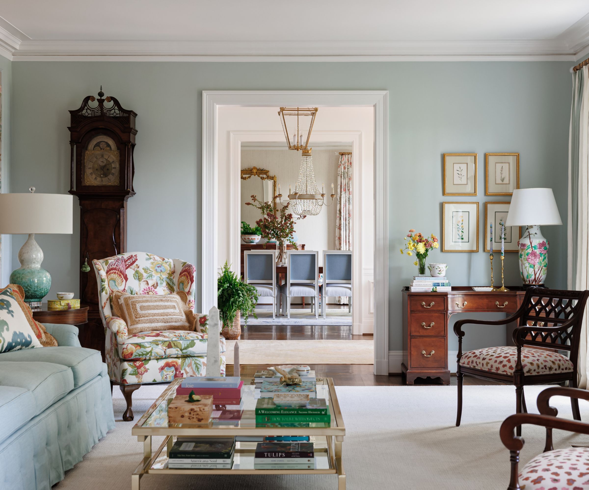 A traditional living room with pale blue walls, vintage and antique furniture, and a cream carpet.