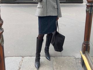 French fashion influencer Sylvie Mus taking a selfie on the street in Paris wearing a chic fall outfit with black knee-high boots.