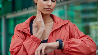 woman looking at her fitness tracker screen while checking her pulse on her neck