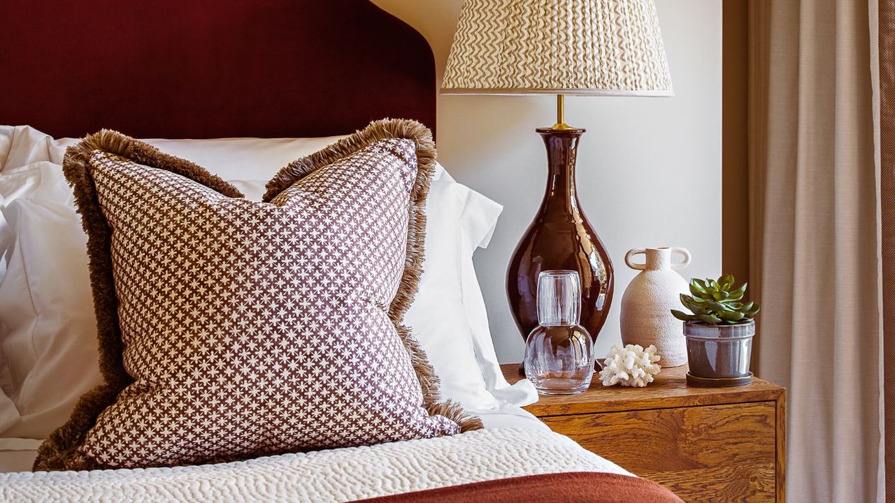 A bed with a red fabric headboard and wooden side table