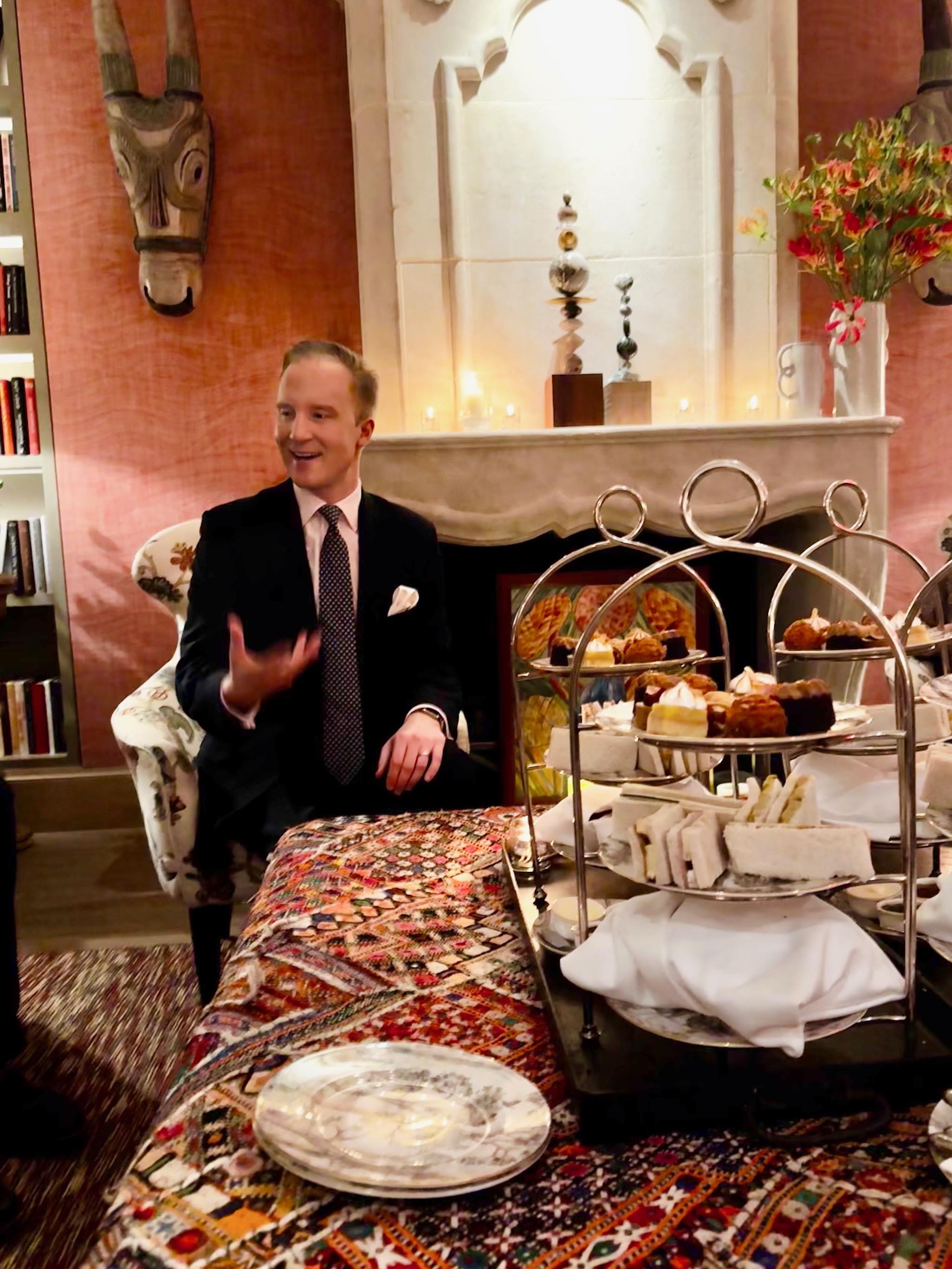 William Hanson wearing a suit sitting in front of a fireplace and afternoon tea trays
