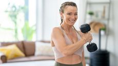 Woman smiles camera as she curls a hex dumbbell to her opposite shoulder