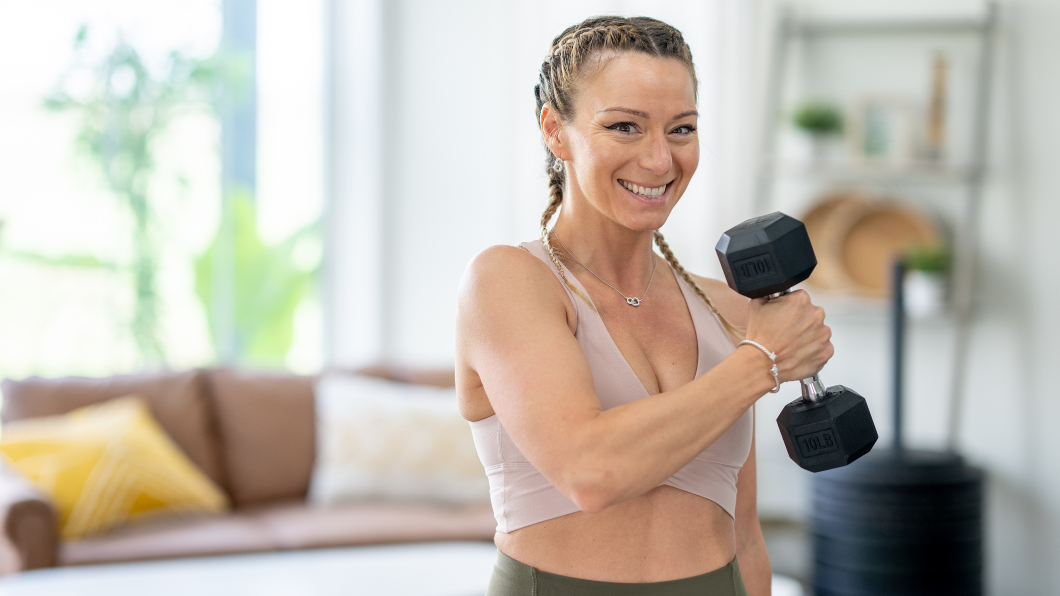 Woman smiles camera as she curls a hex dumbbell to her opposite shoulder
