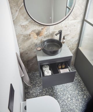 Compact contemporary bathroom featuring a black round vessel sink, sleek vanity with hidden storage, and striking marble-effect walls.