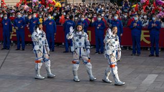 three astronauts in white suits smile and wave to a crowd