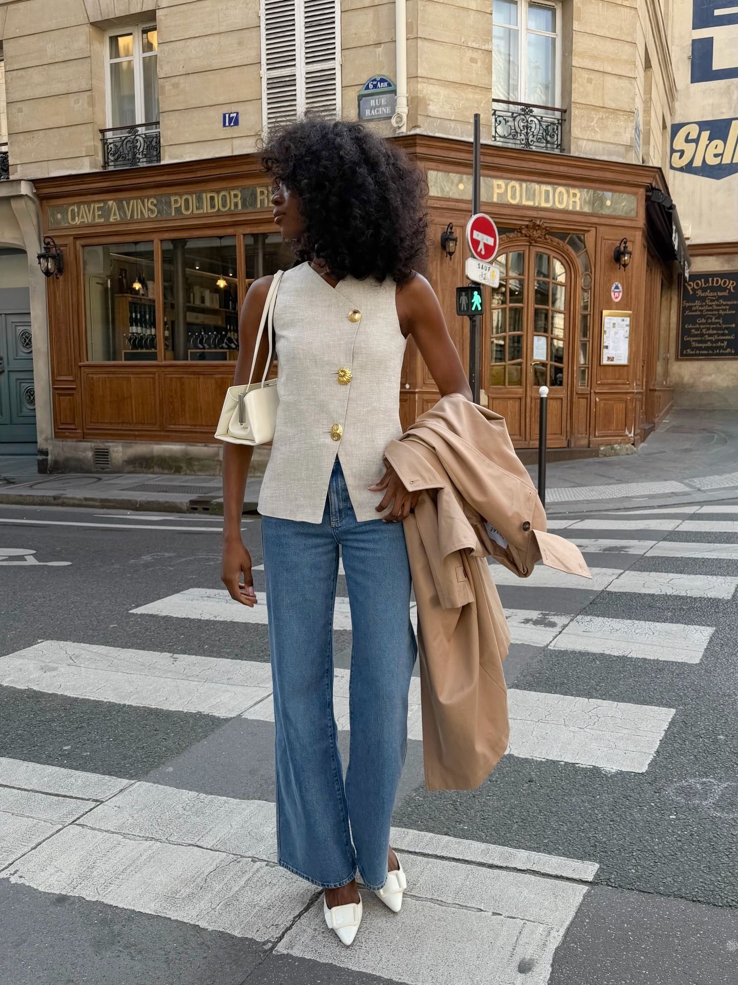 @emmanuellek_ wearing a Sezane high-neck vest, bootcut jeans, trench coat, and East West bag