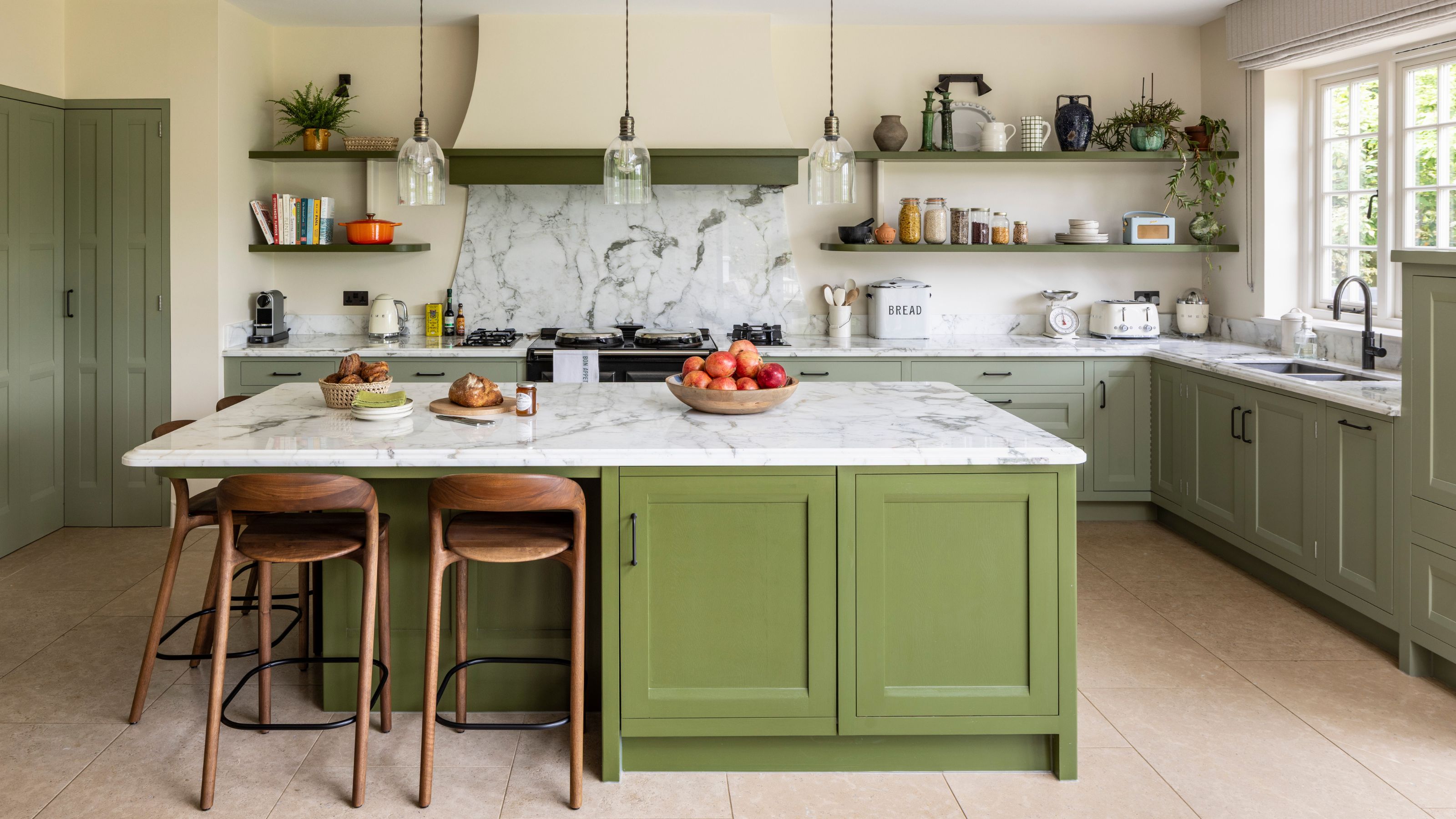 a neutral kitchen with green cabinetry and a brighter green kitchen island with marble counters and wooden stools
