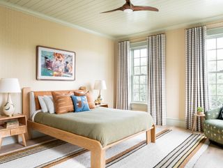 bedroom with wooden bed, green throw, yellow patterned wallpaper, striped rug