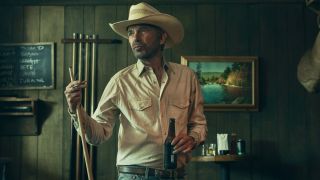 Billy Bob Thornton as Tommy Norris in Landman holding a pool stick and cigarette in his left hand and a beer bottle in his right. 