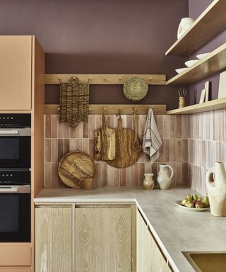 Warm pink kitchen backsplash tiles stacked vertically, teamed with a cement-look cream counter and dark purple paint towards the ceiling