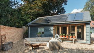 single storey weatherboard building with solar panels on roof and gravelled outdoor seating area with sofa