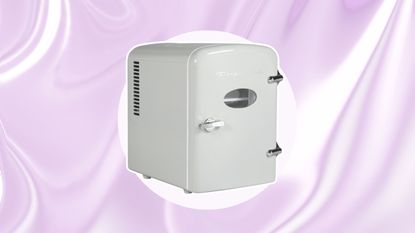 A white retro mini fridge on a purple circle with a purple wavy background behind it