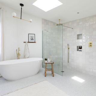 White bathroom with freestanding bath, walk-in shower, gold taps and wooden stool