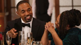 Jason George as Ben Warren laughs with Chandra Wilson as Miranda Bailey as they sit at a table during a firefighters banquet on the May 18, 2024, episode of Station 19, "Glamorous Life."