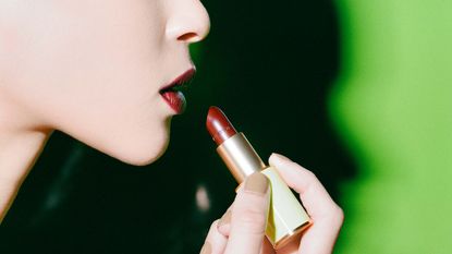 Woman putting on red Dries Van Noten lipstick, illustrating our beauty products round-up