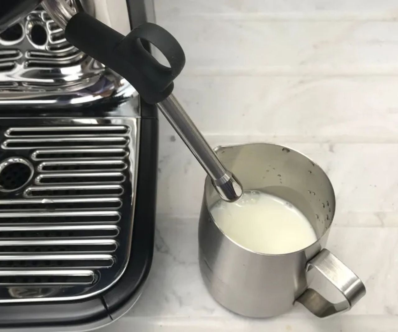 A stainless steel jug of milk beside a steam wand on the Breville Barista pro