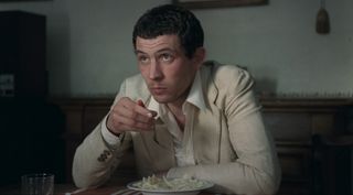 Film still from La Chimera movie showing actor Josh O’Connor in a suit eating pasta