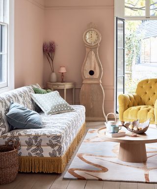 Boho living room ideas illustrated by a patterned, fringed sofa with rug, coffee table, Swedish clock and yellow armchair