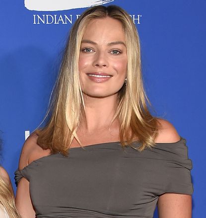 Margot Robbie on a step and repeat wearing a gray mini dress