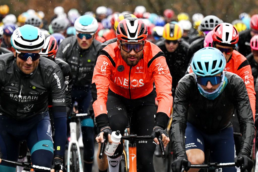 Filippo Ganna (Ineos) bundled up in a red jacket amid the peloton on a cold, rainy stage of Tirreno-Adriatico