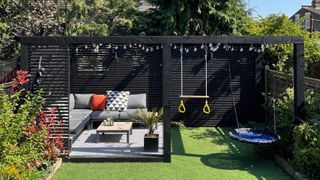 black pergola with kids play equipment at bottom of a garden to block a neighbor's view