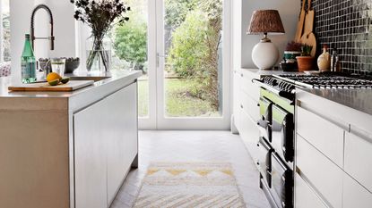 Kitchen with wooden floor, white fitted cabinets and kitchen island, glass door to garden.