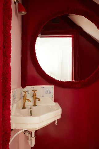 Image of a corner of a bathroom that is drenched in red. The walls are pink and red and there is a mirror with red tufted trim around it and a white sink