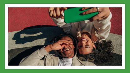 a couple laughing and taking a selfie while on the floor of an outdoor court