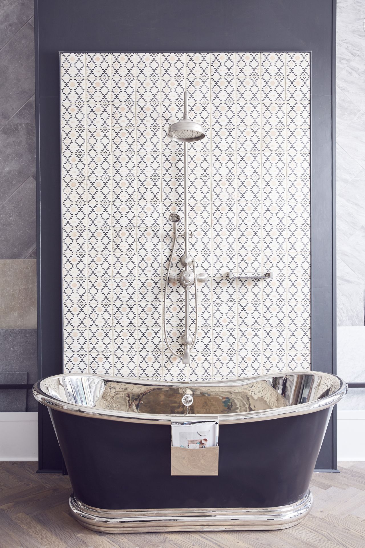 A black and silver bateau bathroom in front of a black and white tiled wall with a shower and water tap installed above the bathtub. Claybrook studio, commercial headquarters and showroom of the tile factory in Shoreditch, London