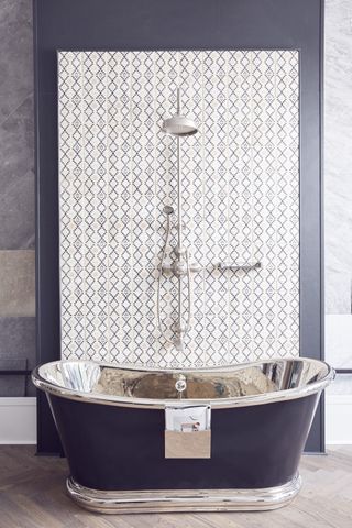 A black and silver bateau bath in front of a wall tiled with black and white tiles with a shower and mixer tap attached over the bath. Claybrook Studio, business premises and showroom of a tile manufacturer in Shoreditch, London