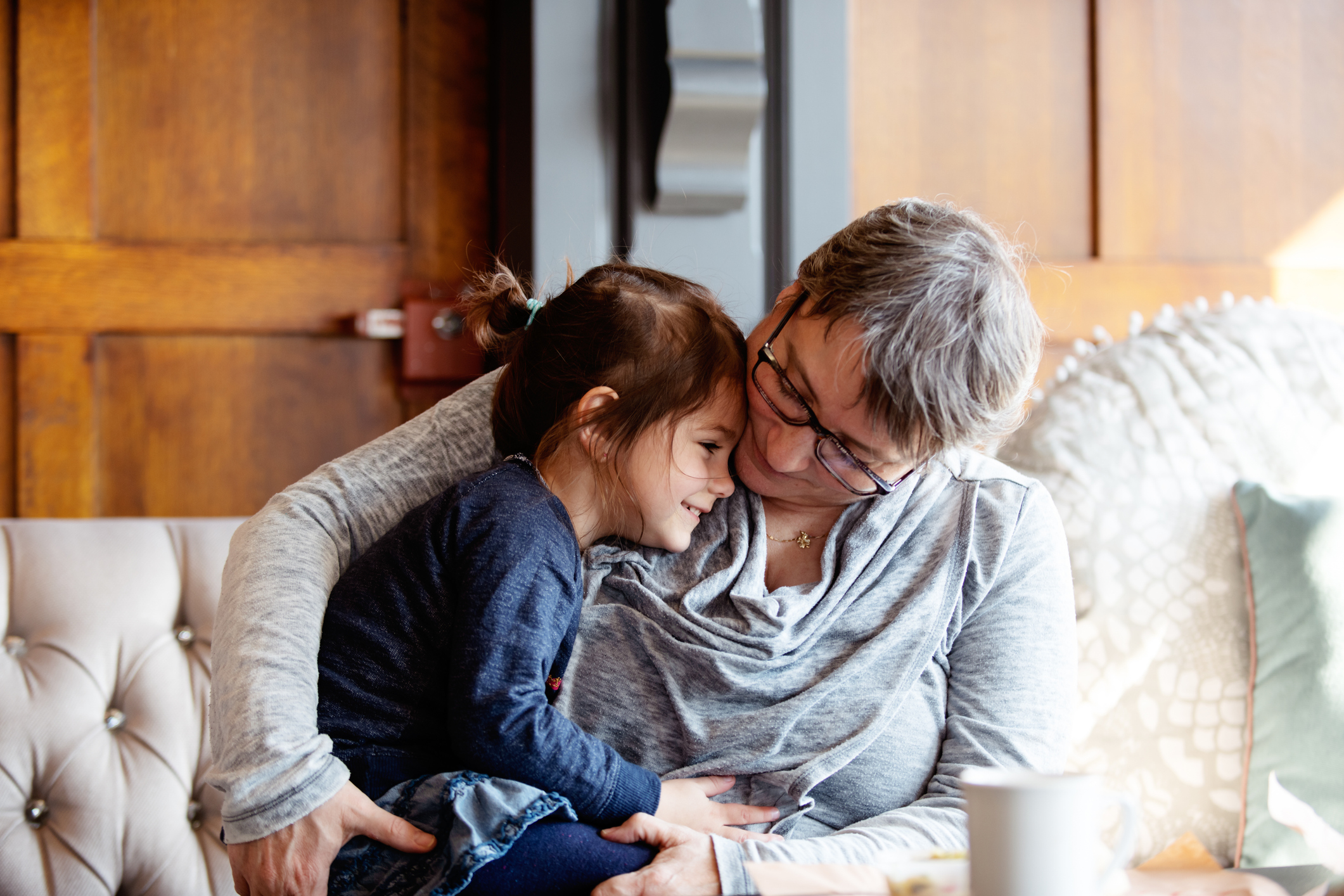 A grandmother hugs her three-year-old granddaughter at a kitchen or cafe table. The photo was taken in Quebec, Canada.