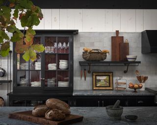 A black kitchen idea with black wood, glass-fronted cabinet and white zellige tiles and marble-topped counter