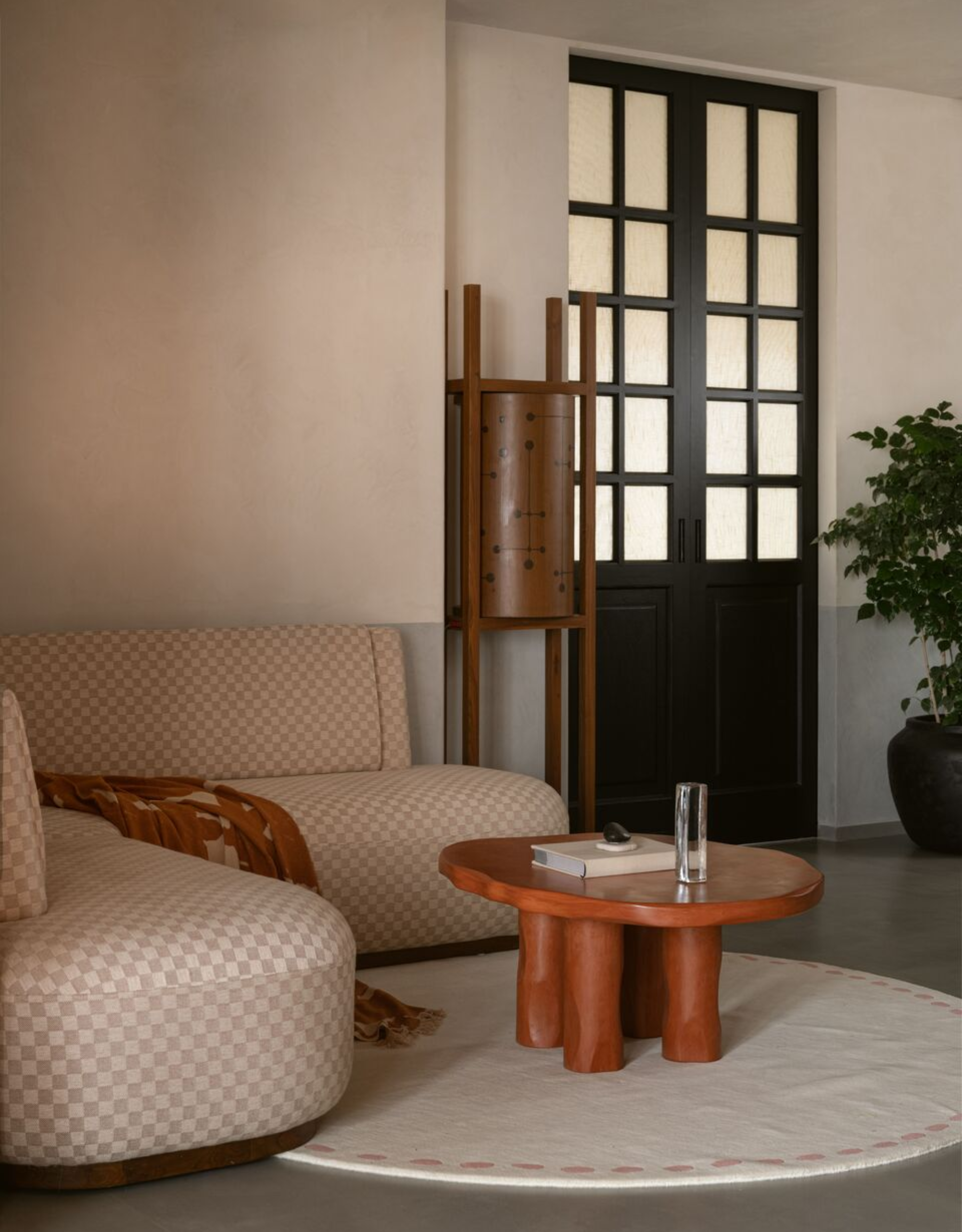 A calm living room with a checkerboard patterned corner couch, a textured wood coffee table, a round rug, and a black door