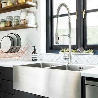 Metal sink and tap by open shelves in kitchen