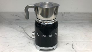 smeg milk frother in black on a marble countertop