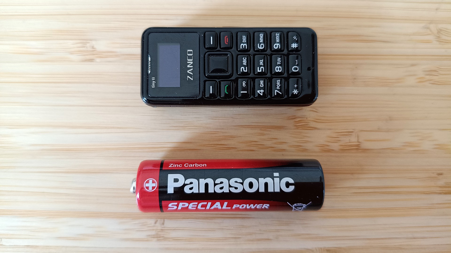 Zanco Tiny T1 phone next to AA battery on desk, to convey their similar sizes