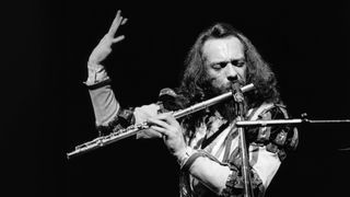 Ian Anderson performing live onstage, playing flute, standing on one leg