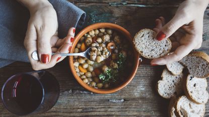 Person eating a high-carb Mediterranean soup with bread