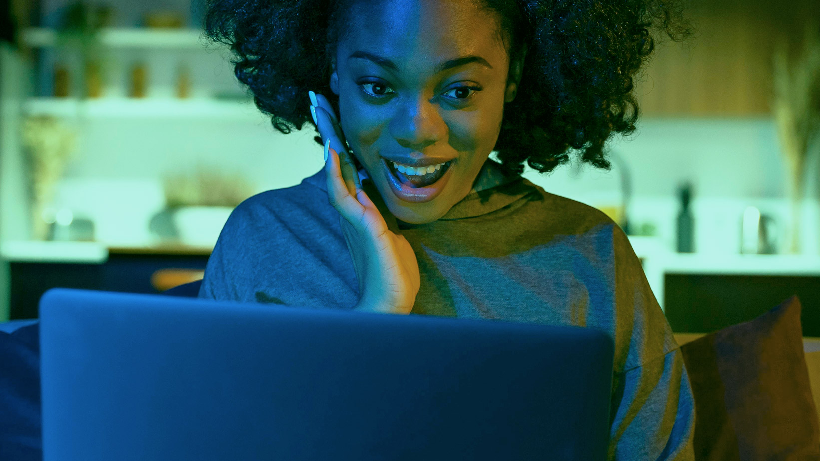 A woman sitting on a sofa and looking at a laptop screen.