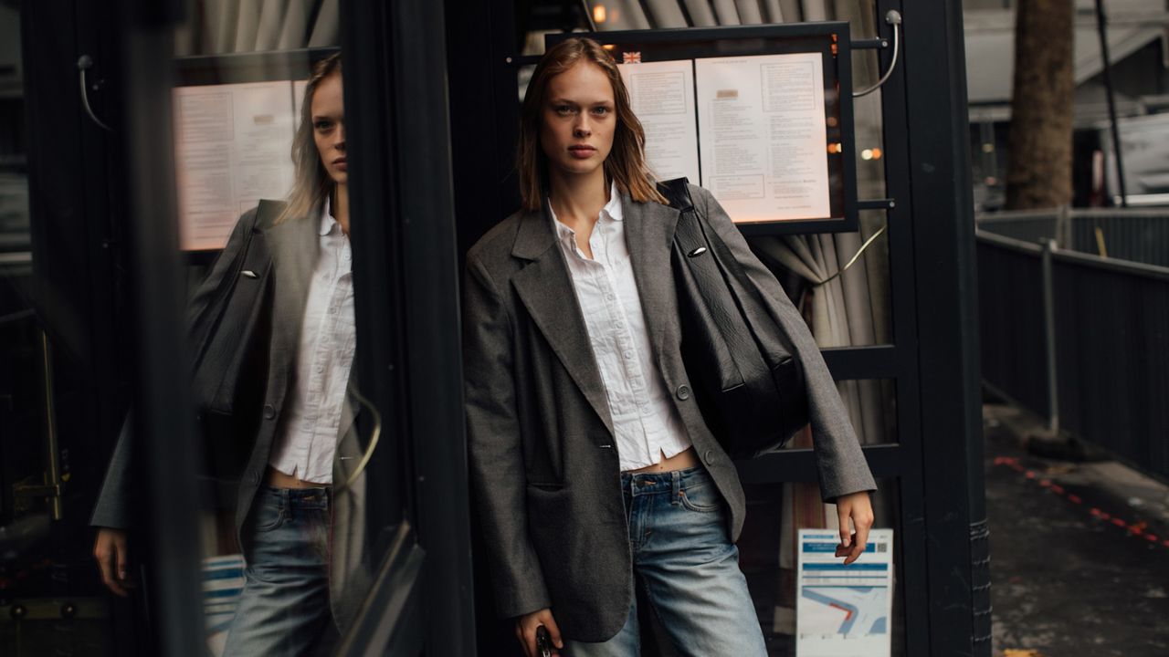 a guest attends paris spring summer 2025 fashion week in a grey blazer black handbag and white button down shirt 