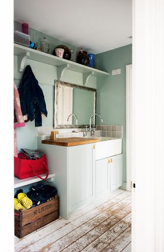 Bootroom with white porcelain sink, large mirror and sage green walls