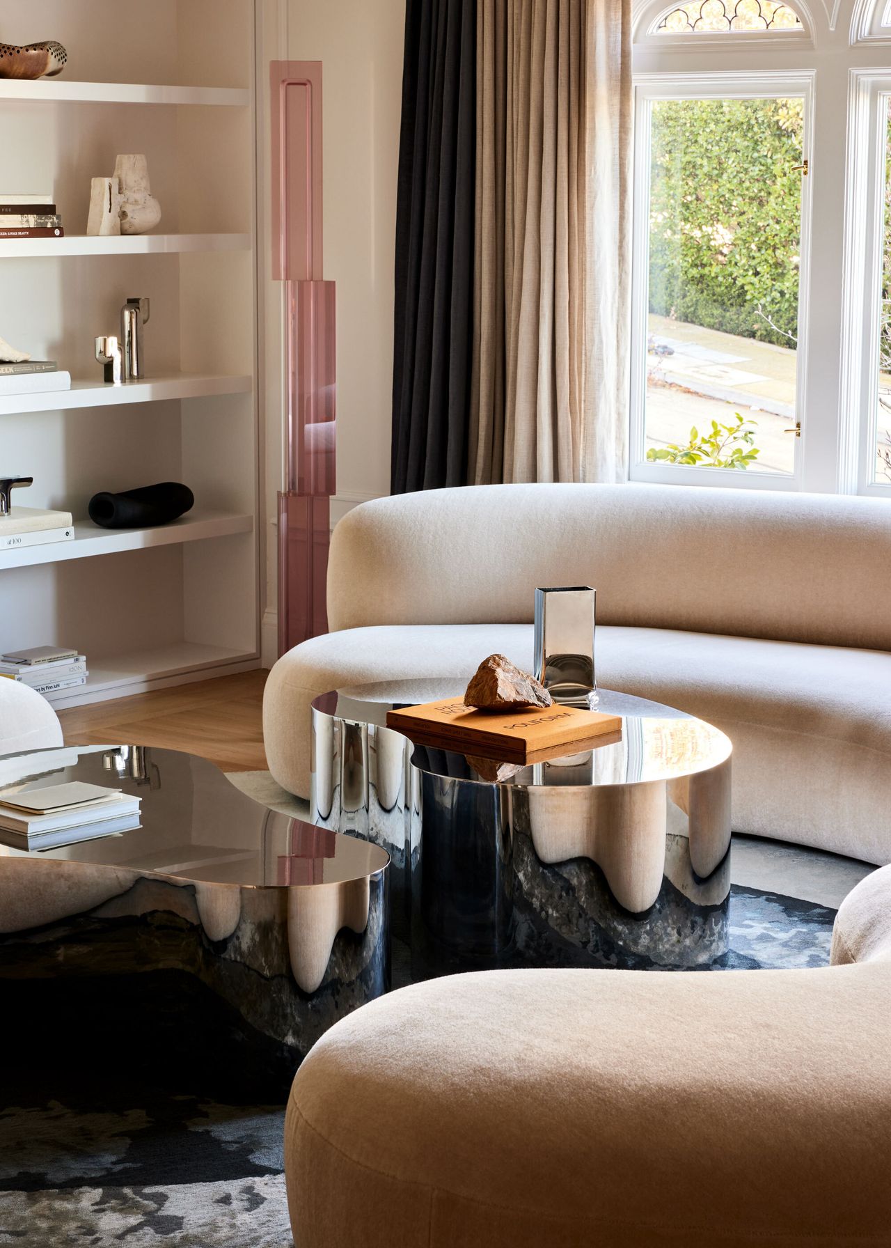 The living room of a San Francisco renovation with curved blush pink couches and statement silver coffee tables